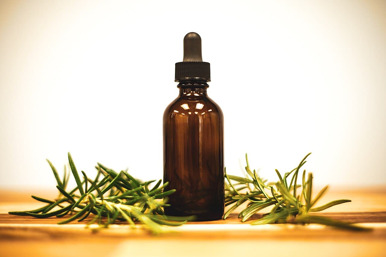 Amber glass bottle of herbal oil surrounded by fresh herbs