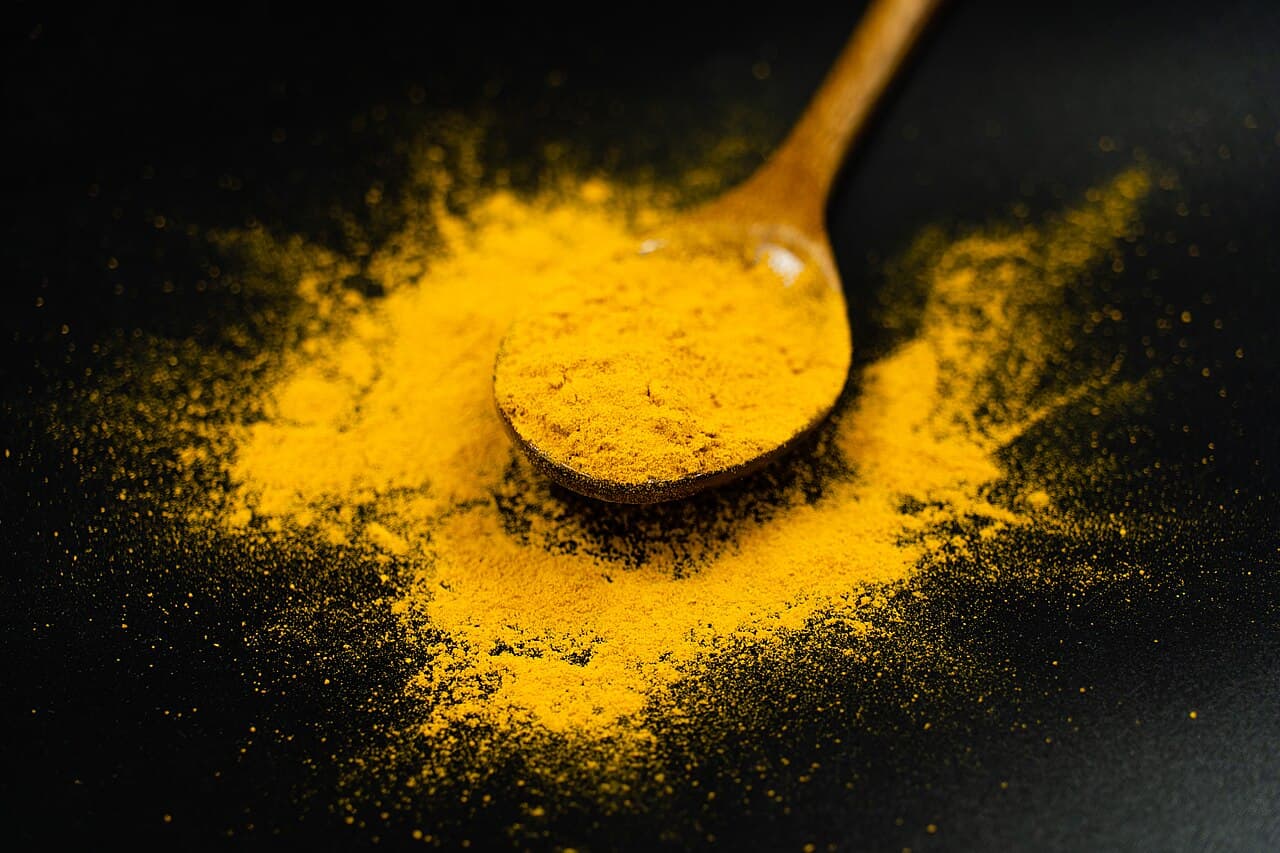 Golden turmeric powder on a wooden spoon against a black background